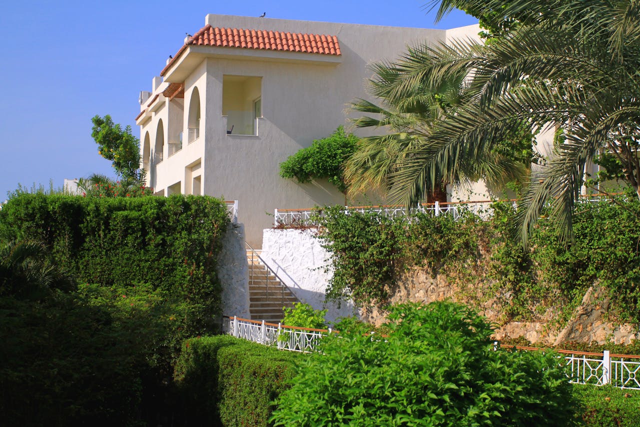 Elegant Mediterranean villa surrounded by lush greenery and vibrant garden landscape.